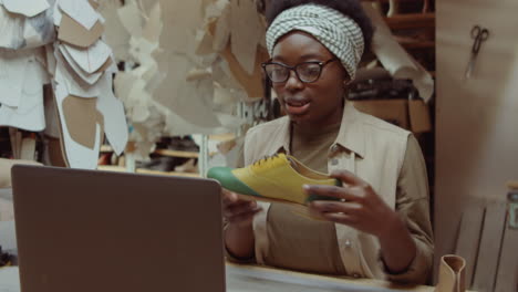 african american woman talking on video call in shoemaker workshop