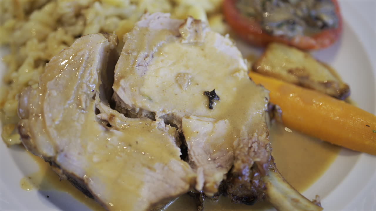 Close up of a portion of egg noodle near a few pieces of pork, cooked carrot and stuffed tomato on a white plate