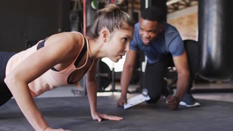 video de un entrenador afroamericano motivando a una mujer caucásica para hacer flexiones