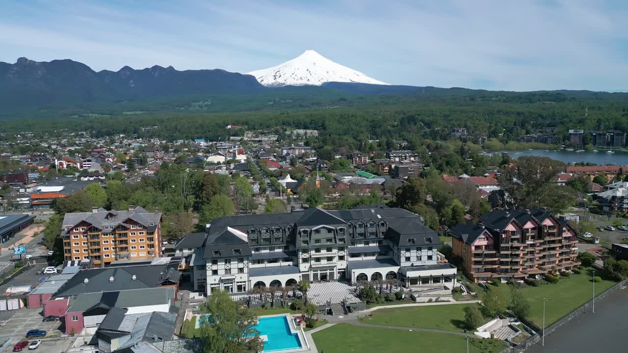 Panoramic drone view of downtown Pucón, with the snow-covered Villarica volcano in the background and scenic architecture along the lake shore