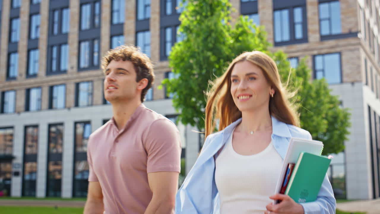 Confident colleagues walking together with notebooks enjoying sunny day closeup