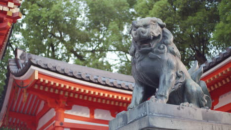 Stone-lion-statue-surrounded-by-a-shrine-and-tall-trees-in-the-background-in-Kyoto,-Japan-soft-lighting