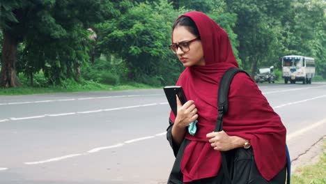 Beautiful-serious-young-Afghan-woman-in-hijab-holding-file-and-bag-in-hand-and-standing-on-street-near-road,-charming-female-in-black-t-shirt