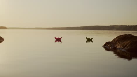 paper boats swim at sunset. evening water background and two origami ships floating. dreams and future concept.