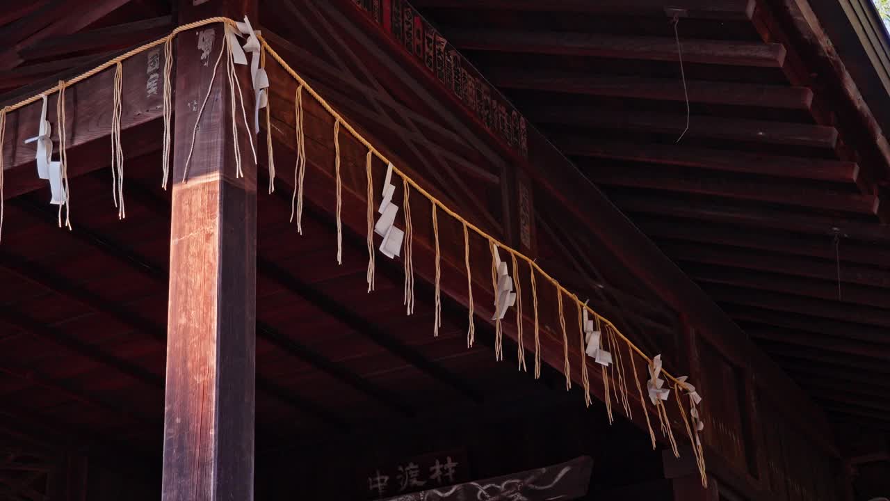 A close-up of shide (folded paper strips) hanging from a rope under a traditional wooden Japanese roof. This detail highlights the sacred and cultural elements of a temple.