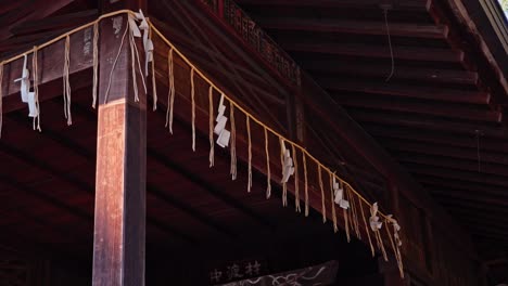 a close-up of shide (folded paper strips) hanging from a rope under a traditional wooden japanese roof. this detail highlights the sacred and cultural elements of a temple.