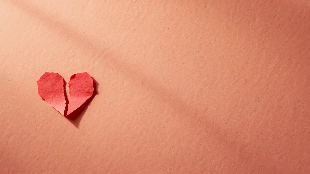 Un cuore di carta rosso strappato a metà, con le due metà che si allontanano su un foglio rosa a partire dallo strappo centrale