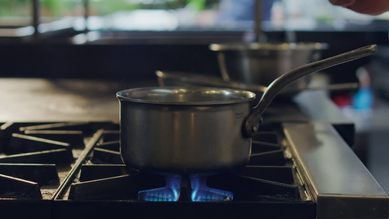 Close-up of a chef cooking ravioli in a pot of hot water over a professional stove fire