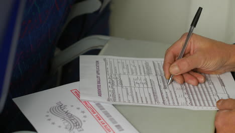 filling out an absentee ballot application with a pen, while the "official election mail" envelope rests nearby. the image highlights the process of completing a mail-in voting form during travel