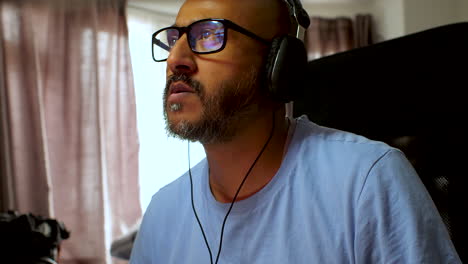 South-Asian-man-with-glasses-and-headphones-working-from-home,-showing-screen-reflections-on-glasses