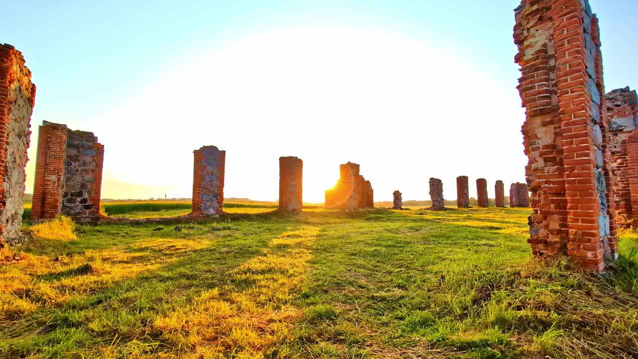 Brick ruins of old building remains in green field under bright golden sunset sky