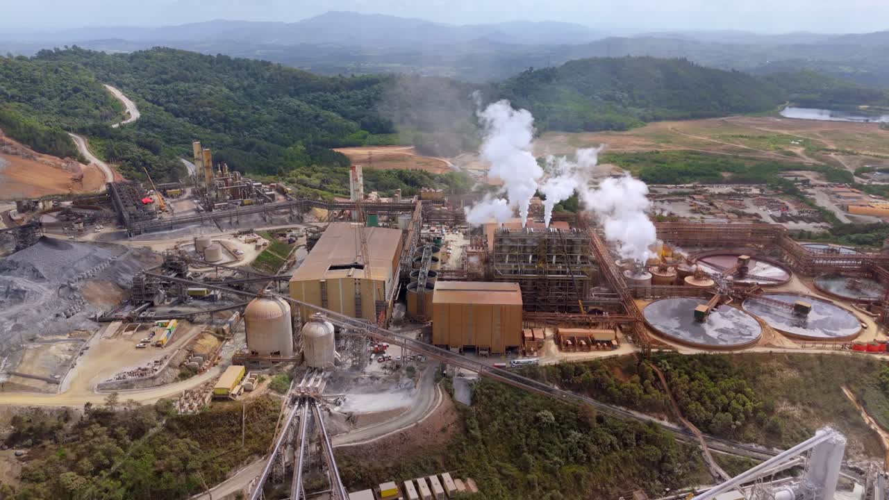 Industrial gold-silver mine with rising smoke from smokestacks. Aerial top down shot. Pueblo Viejo Mine in Cotui, Dominican Republic. Green forest landscape in distance.