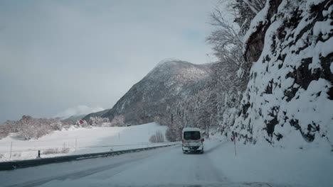 POV-video-of-a-daytime-drive-through-the-snowy-roads-of-Norway's-Western-Fjords,-surrounded-by-tall,-snow-covered-mountains-with-trees