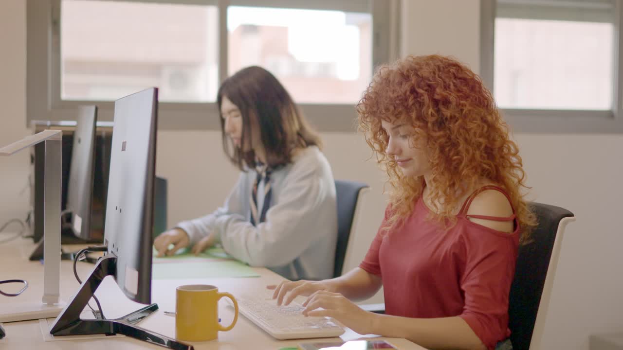 Woman with curly hair working concentrated next to a mate