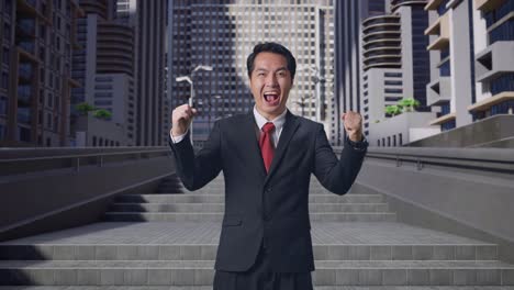 幸せなアジア人ビジネスマンが街で立って祝っている