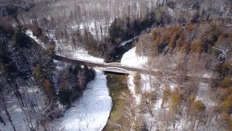 puente panorámico con un camino sinuoso que se extiende por un río ancho en un paisaje invernal con nieve y árboles de hoja perenne