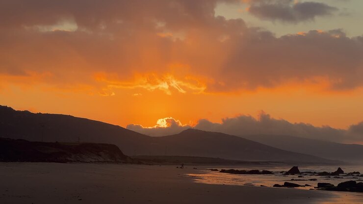 Una puesta de sol dorada detrás de una colina con vistas a una hermosa playa de arena