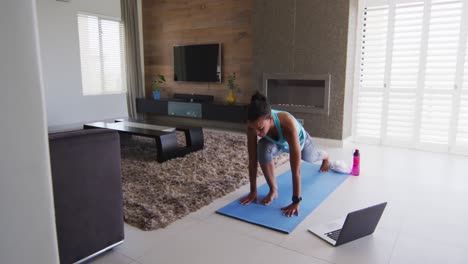 mujer de raza mixta haciendo ejercicio en una alfombra con computadora portátil