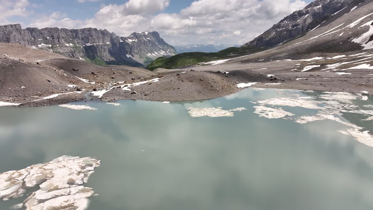 스위스 알프스 산맥 한가운데의 산과 하늘을 반영하는 크리스탈 은 호수 위를 천천히 날아가는 무인기 이미지