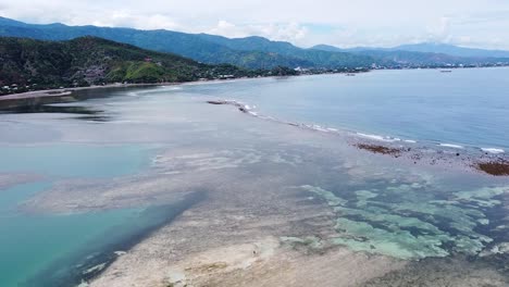Aerial view flying over solo fisherman in ocean at low tide with coral reef and sand bars on tropical island of Timor-Leste, Southeast Asia
