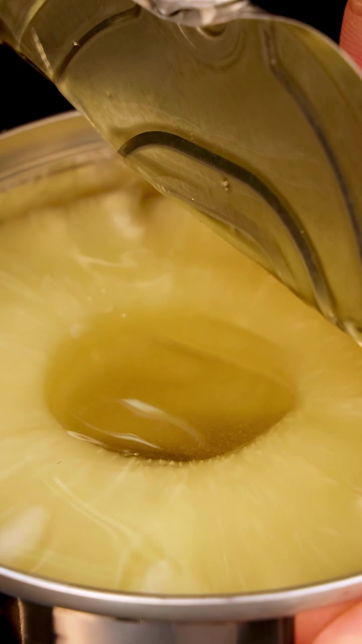 A hand opens a canned pineapple using a pull tab, revealing pineapple rings inside. Macro close-up, bright studio lighting, steady camera, high detail