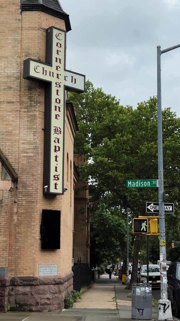 Pedoni camminano oltre una chiesa storica e cartelli stradali su un marciapiede della città di Brooklyn