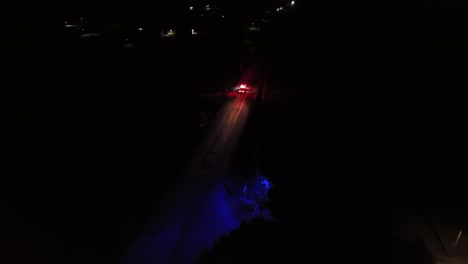 fire truck arriving accident on highway at night. aerial wide shot. flashing red lights and blue light in american suburb forest.