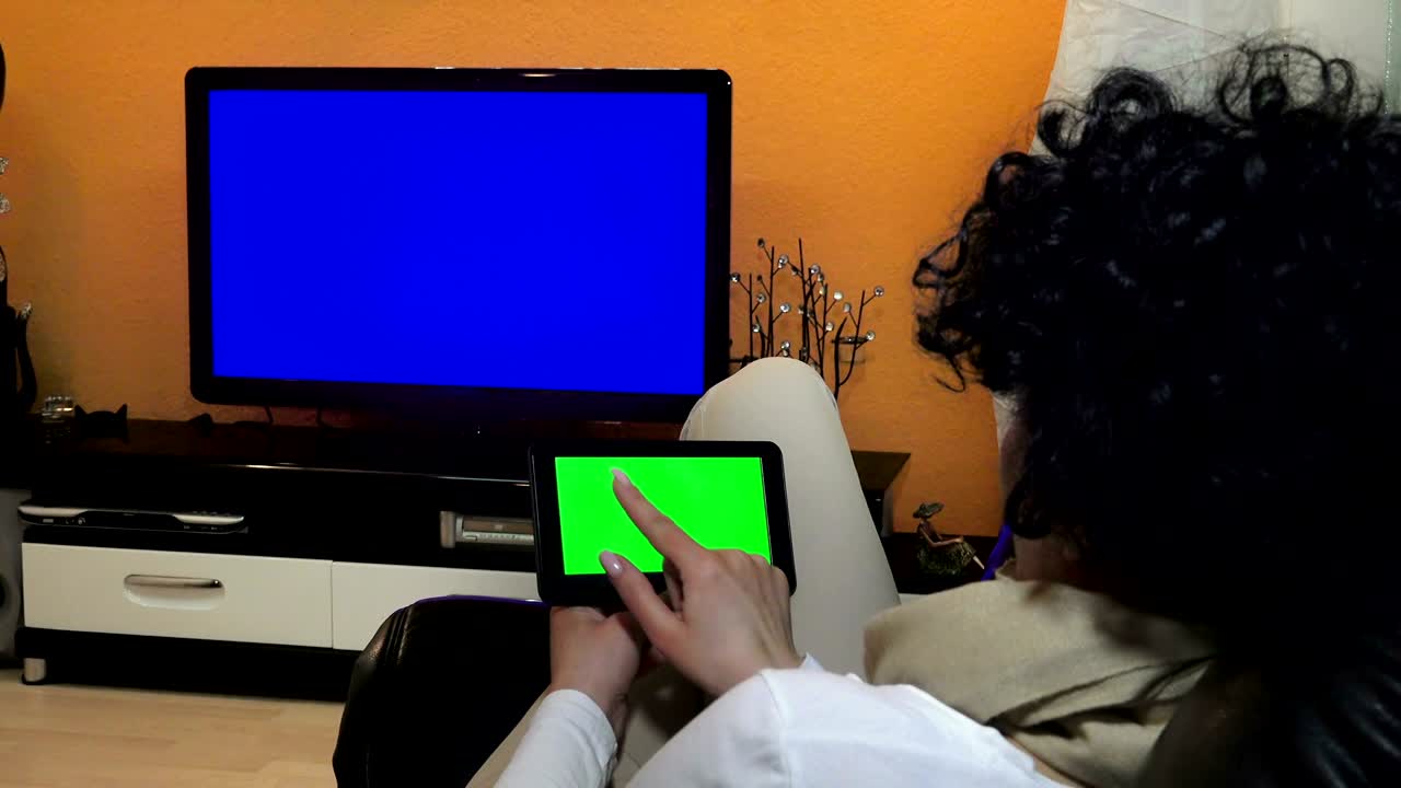 mujer mira la televisión mientras sostiene y toca en un dispositivo de tableta. uhd stock video con luma matte