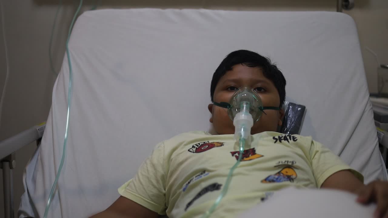 Paziente ragazzo asiatico che riceve una maschera d'ossigeno, sdraiato su un letto d'ospedale