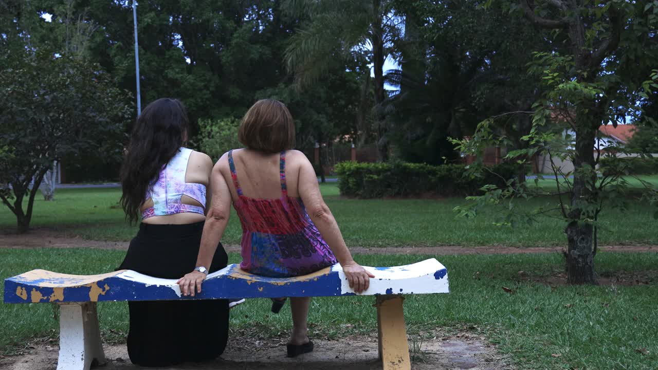 madre e hija sentadas en un banco en el parque hablando entre ellas y relajándose con un sutil movimiento de cámara deslizante