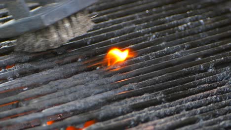 un cepillo de alambre limpia una parrilla mientras una pequeña llama arde sobre algunos alimentos viejos en cámara lenta