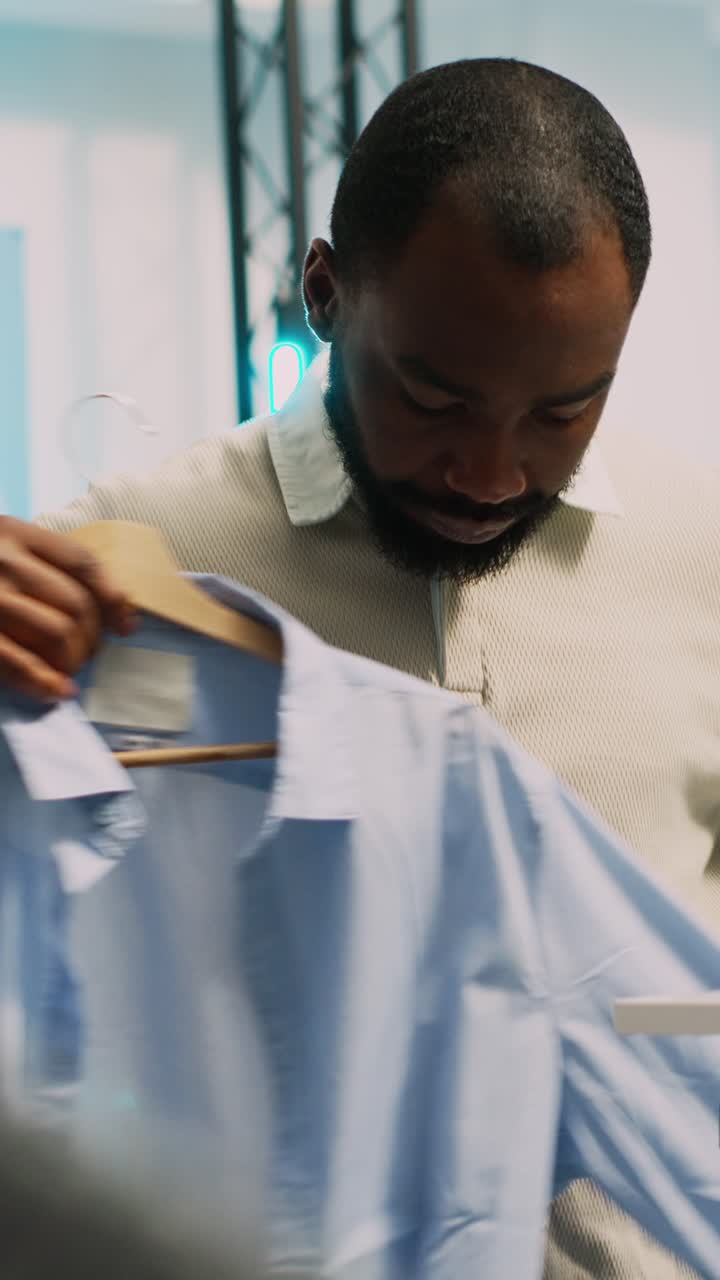 Vertical video: Male retail customer picking up clothes from racks