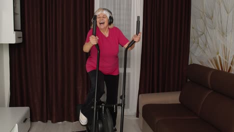 Senior-woman-in-sportswear-using-orbitrek-listening-music-at-home-doing-sport-cardio-exercises