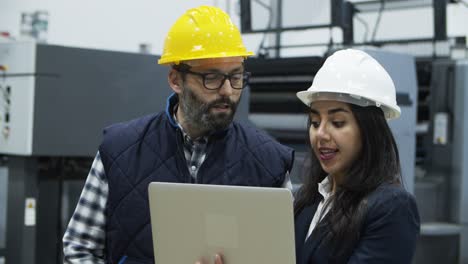 focused factory employees talking while standing with laptop