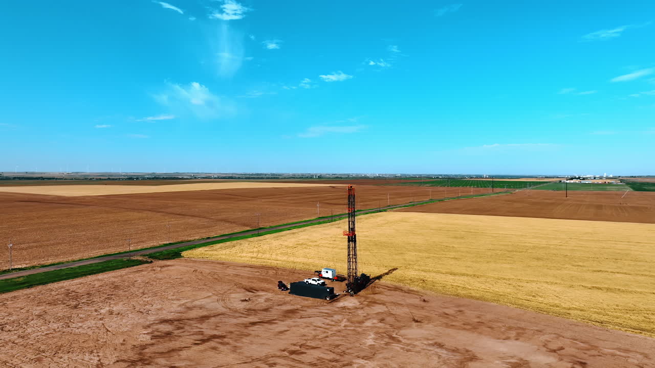 Footage above the vast field with little site for oil extraction. Cars and wagons stand around the truck with set derrick. Aerial view.