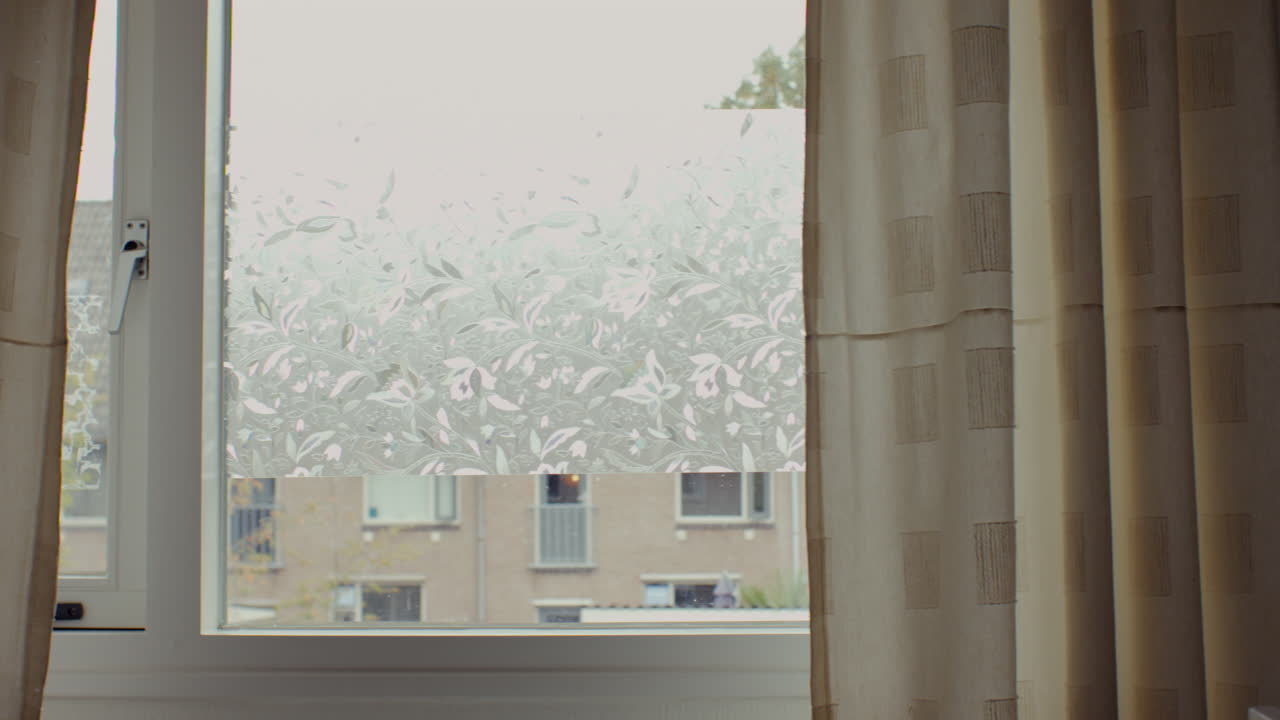 Calm indoor view through a window with patterned frosted glass in the Netherlands. The frame captures curtains, soft daylight, and subtle architectural details in a quiet residential neighborhood