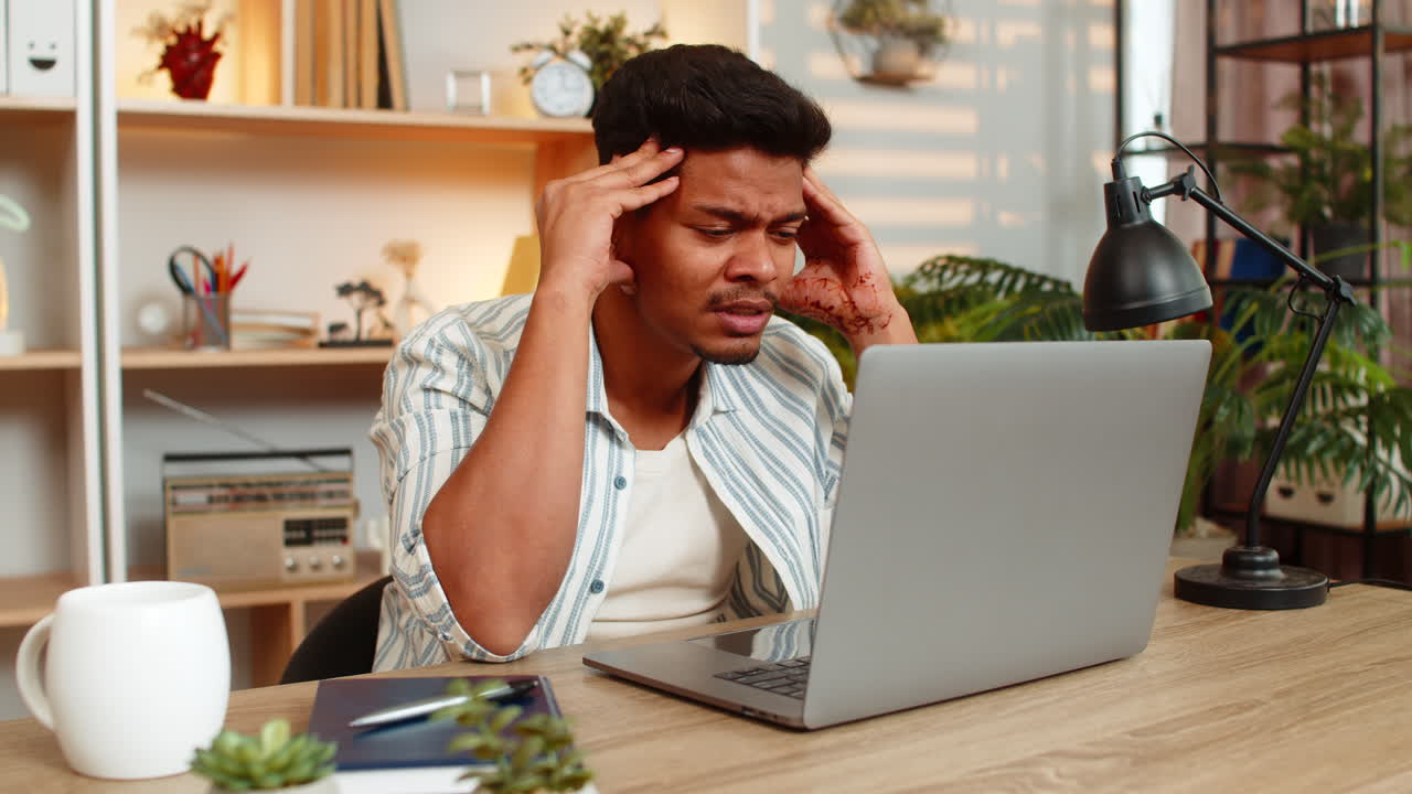 Indian man on home table looking at laptop screen and thinking seriously during focused remote work