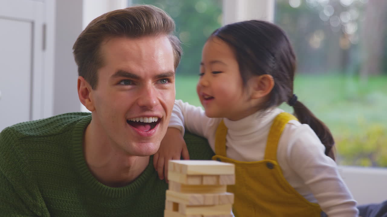 Daughter Whispering In Parent's Ear As Family With Two Dads Play Game Stacking Wooden Bricks