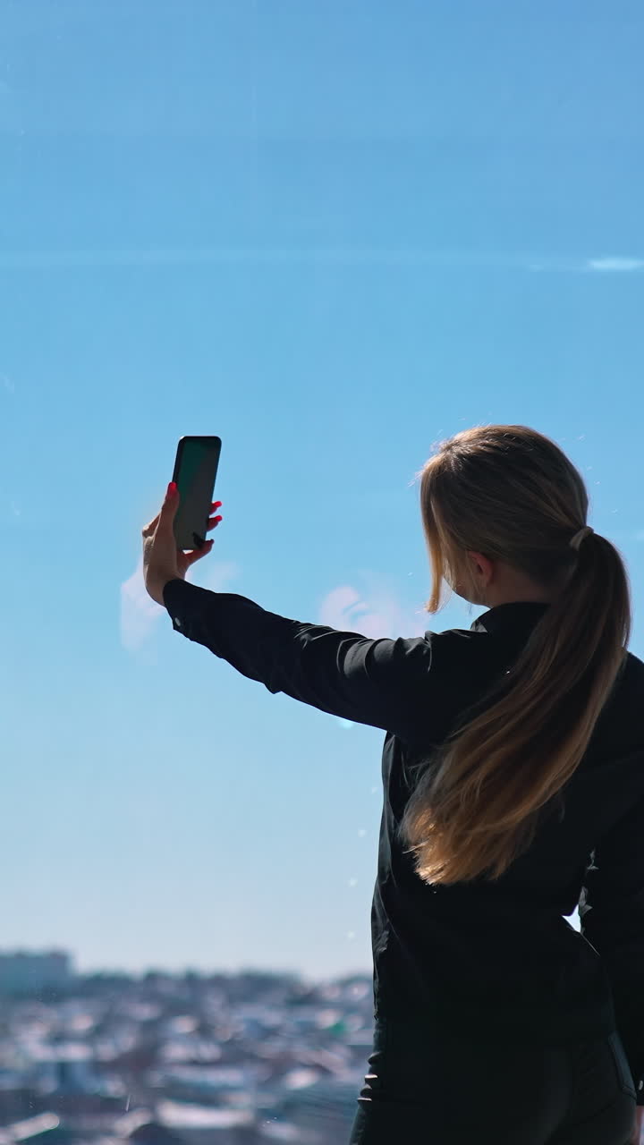 Lovely business woman in black taking photo of herself. Beautiful young woman doing selfie on smartphone while standing at office window. Vertical video