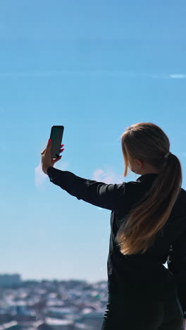 lovely business woman in black taking photo of herself. beautiful young woman doing selfie on smartphone while standing at office window. vertical video