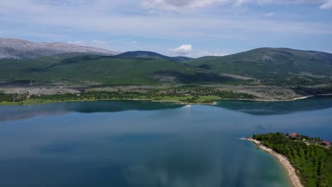 a lake in northern croatia surrounded by greenery and mountains on a bright partly cloudy day