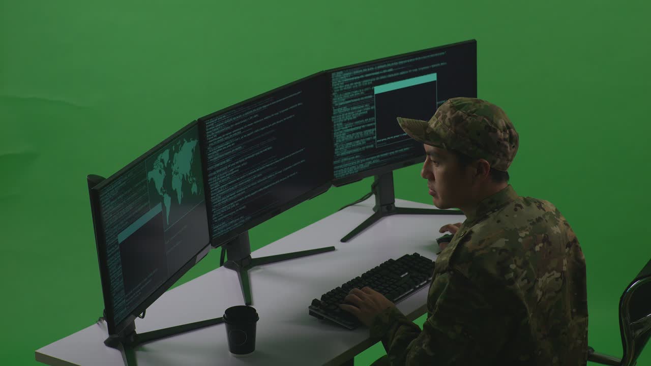 Side View Of Asian Man Soldier Developer Drinking Coffee And Using Computer To Write Code With Multiple Screens In Green Screen Studio