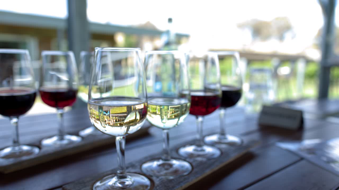 Un’ampia inquadratura statica cattura diversi calici di vino su un tavolo di legno in una cantina vinicola