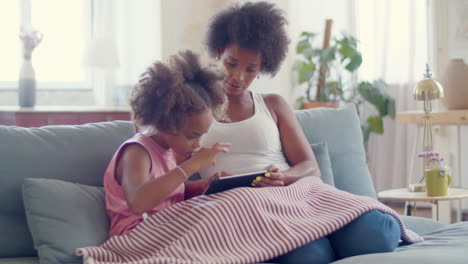 concentrated black woman helping cute daughter in studying online on digital tablet