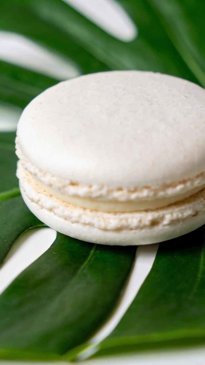 Vertical video: Zooming camera centering macaron on table with monstera leaf, showing detail