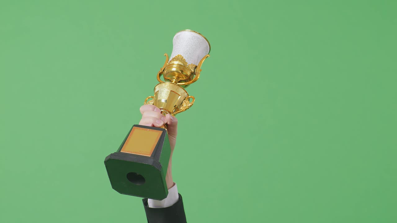 cerca de la mano del hombre de negocios sosteniendo un trofeo de oro en el aire para celebrar la victoria como el primer ganador en el fondo de la pantalla verde en el estudio
