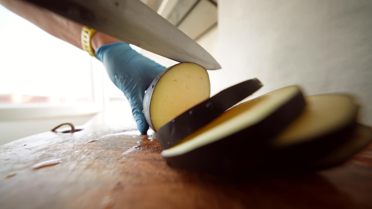 Close-Up of Hand Slicing Fresh Eggplant on a Wooden Cutting Board