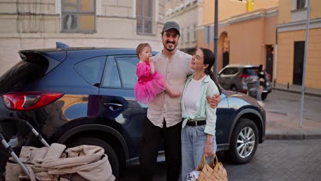 una feliz familia de tres personas de pie junto a su coche en la ciudad