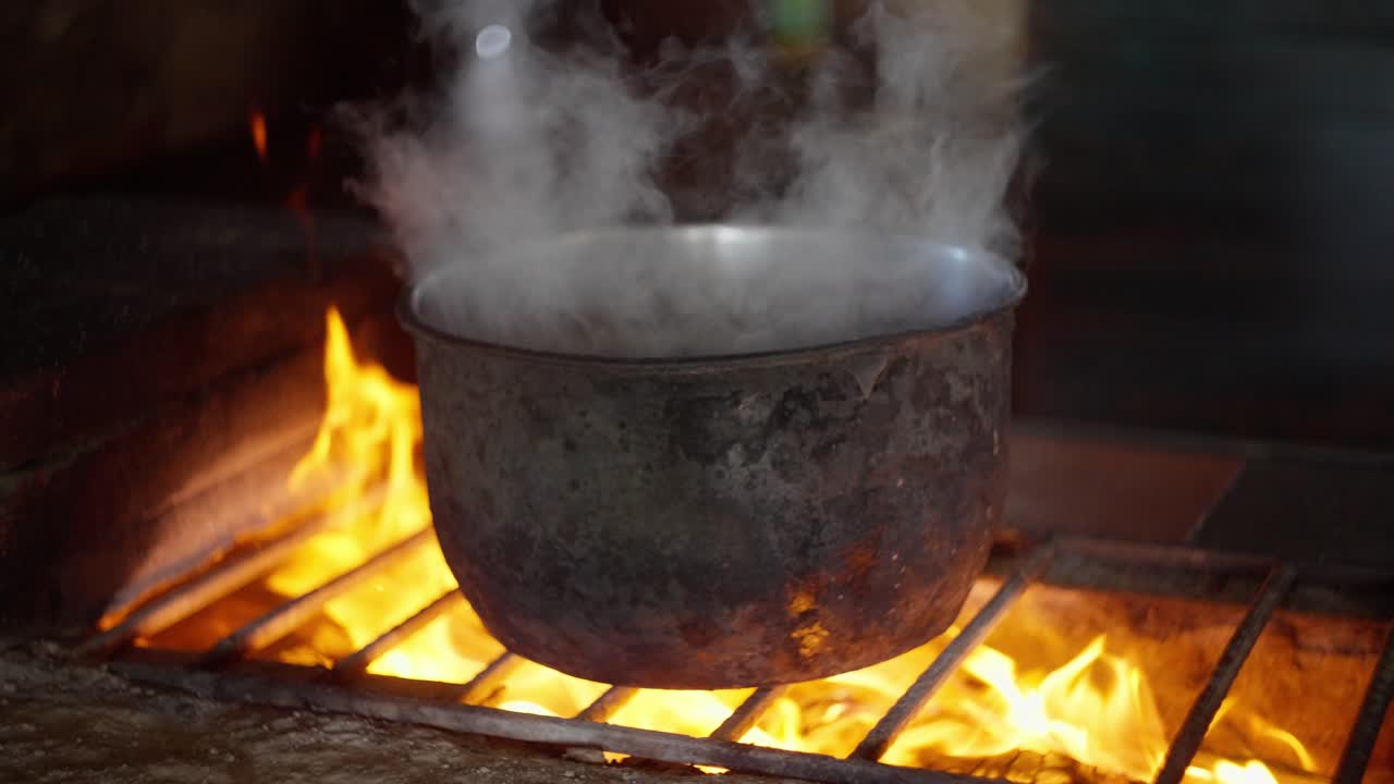 Slow Motion view of the smoke coming out from a metal worn out pot placed in a rudimentary wood stove with the flames bursting.