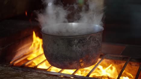 slow motion view of the smoke coming out from a metal worn out pot placed in a rudimentary wood stove with the flames bursting.